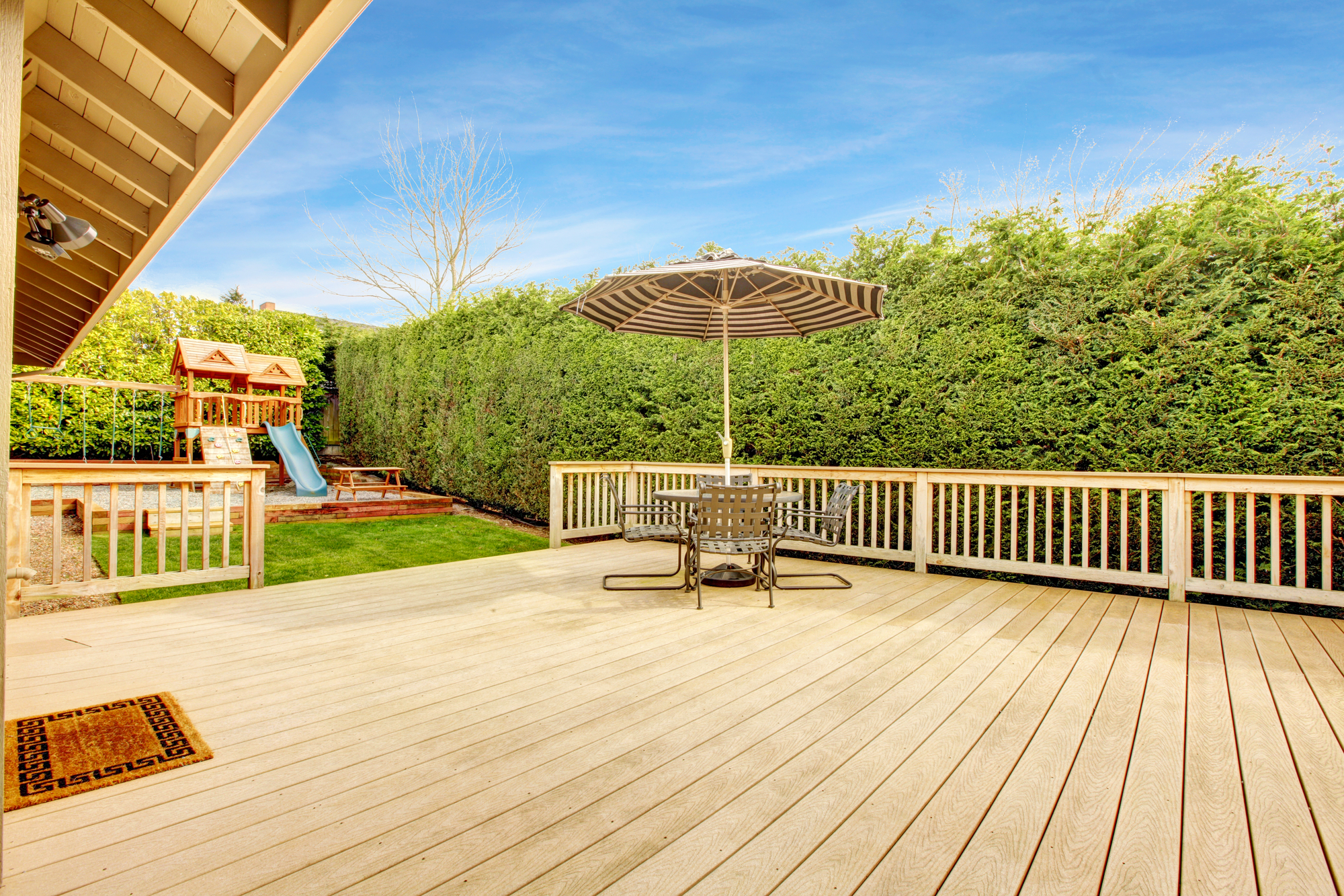 Bakyard with patio area and play yard for kids Spacious wooden deck with umbrella and patio table set. View of play yard with chute